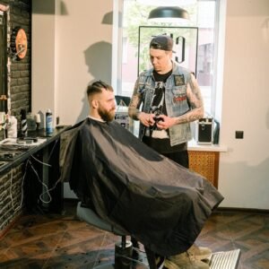 A tattooed barber styling a client's hair in a trendy salon setting.